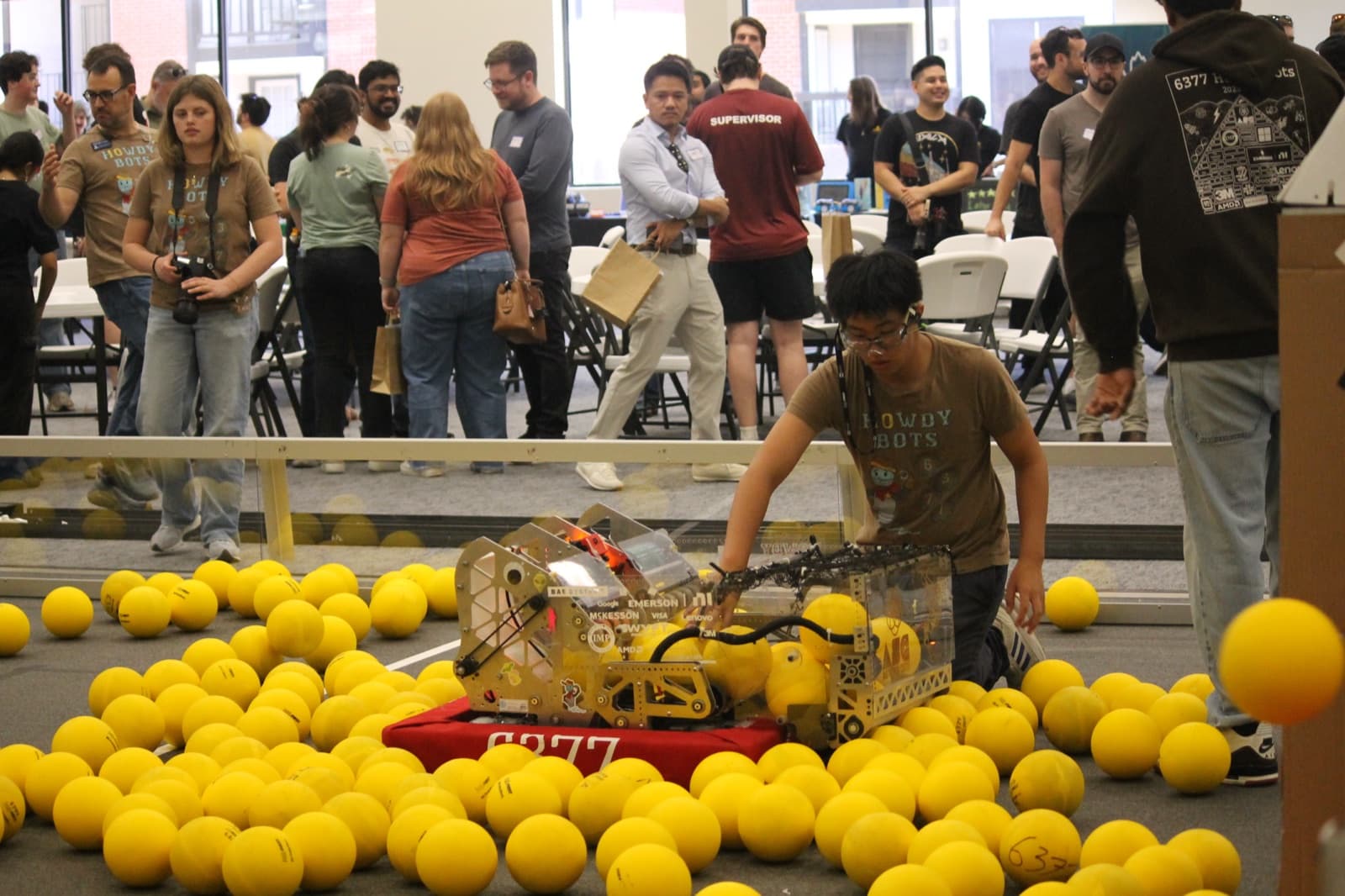 A student drives a FIRST Robotics robot through a field of yellow balls while a crowd watches at the Austin STEM Center grand opening