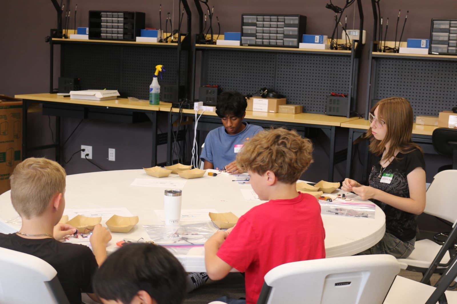 Campers assembling electronics from parts trays around the table
